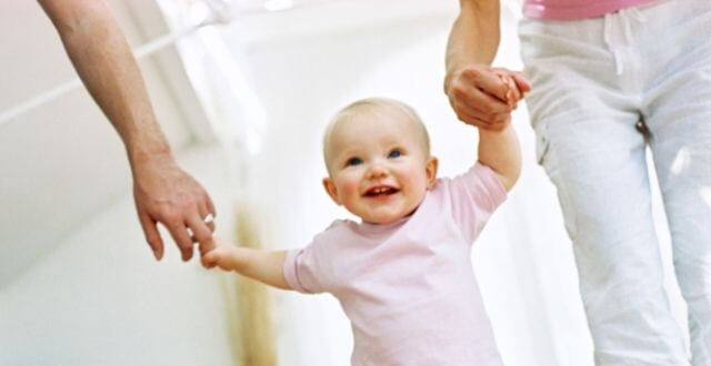 happy toddler walking between parents holding their hands