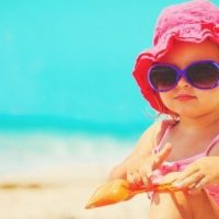 toddler girl at the beach in bright pink hat and sunglasses